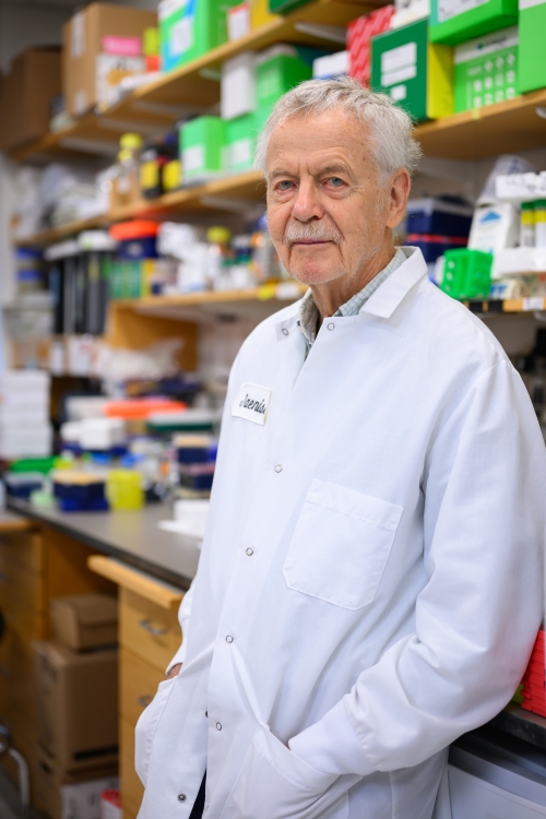 Rudolf Jaenisch in lab coat leans against a bench in the lab