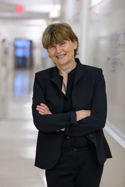 Ruth Lehmann in a black suit stands in a bright hallway, smiling at the camera