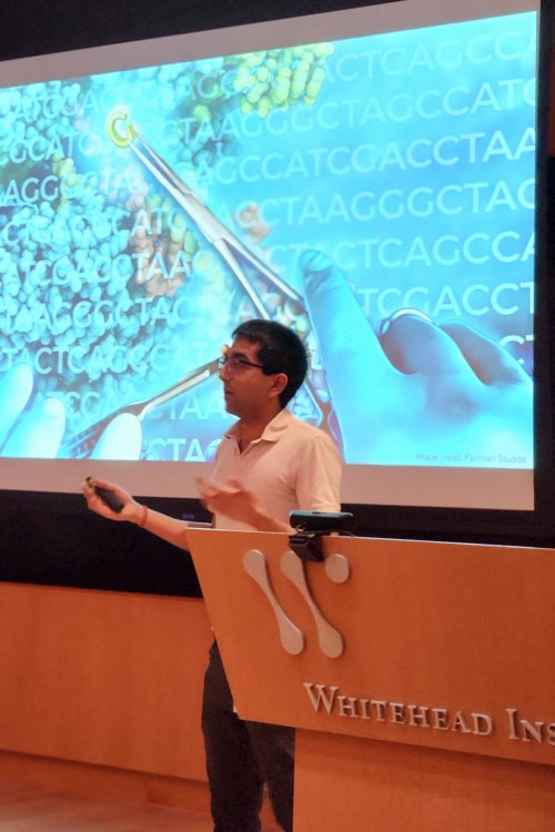 A man speaks in front of a projector showing someone cutting DNA sequences with scissors, with a Whitehead Institute lecturn visible in the corner