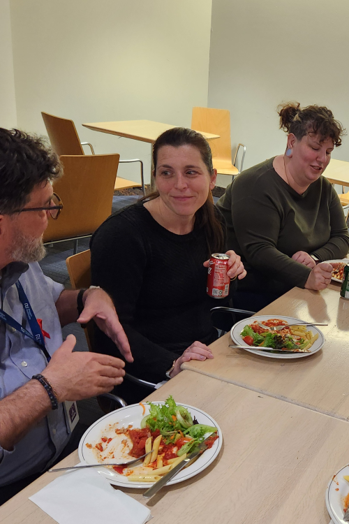 Three adults sit next to each other at a table, chatting and eating dinner