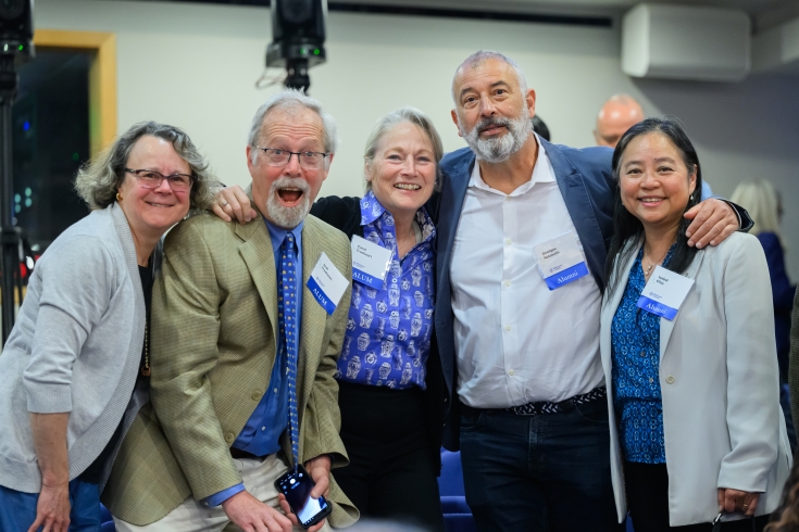 A groupf of five people stand with arms around each other in a line and smile happily at the camera