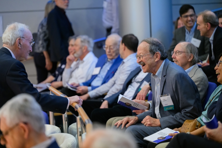 Gerry Fink speaks to a friend in the audience, who leans forward from his seat to talk