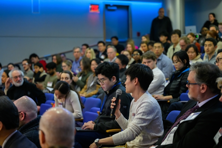 A packed auditorium. One attendee holds a microphone to ask a question