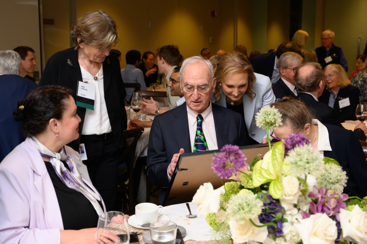 Gerry Fink looks at a plaque he's received, sitting at a reception table, while others look on