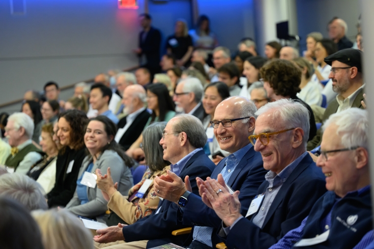 A packed auditorum claps and smiles