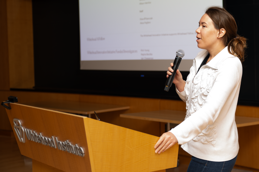 Allison Hamilos with microphone in hand, speaks in front of a large slide on a screen