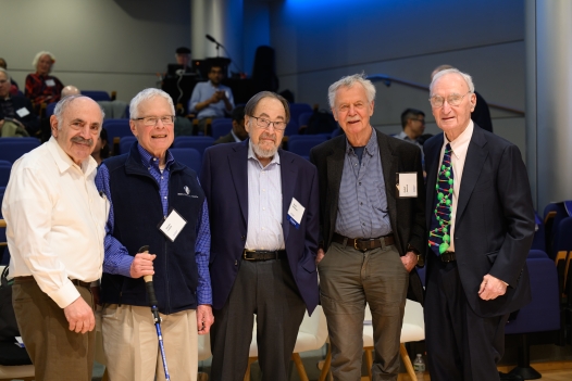 Five elderly men stand in a row together looking at the camera